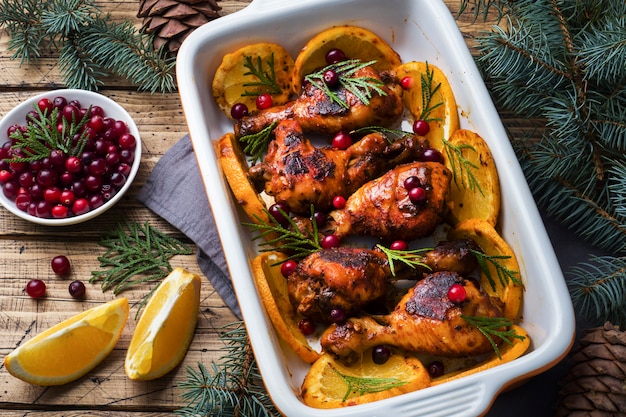 Coscia di pollo al forno con arance e mirtilli rossi in una teglia su un fondo di legno.