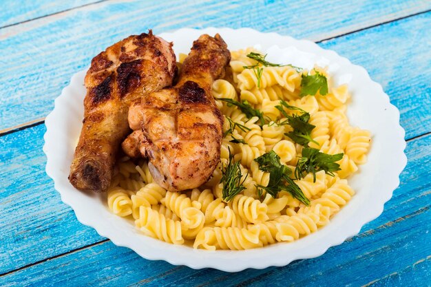 Coscia di pollo alla griglia e pasta su fondo di legno blu piatto bianco