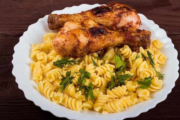 Coscia di pollo alla griglia e pasta su fondo di legno marrone del piatto bianco