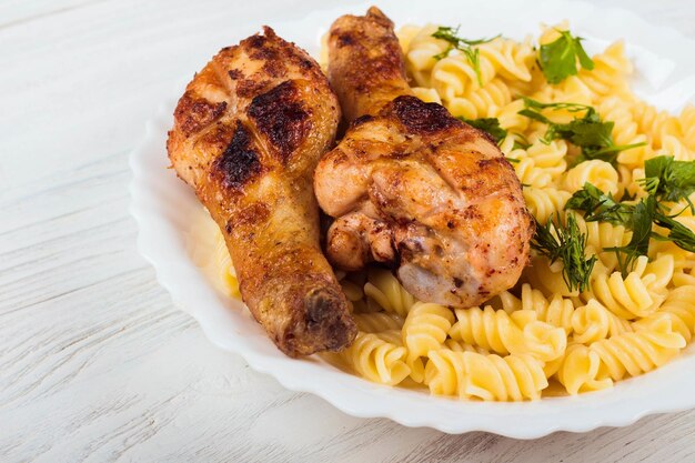 Coscia di pollo alla griglia e pasta su fondo di legno piatto bianco