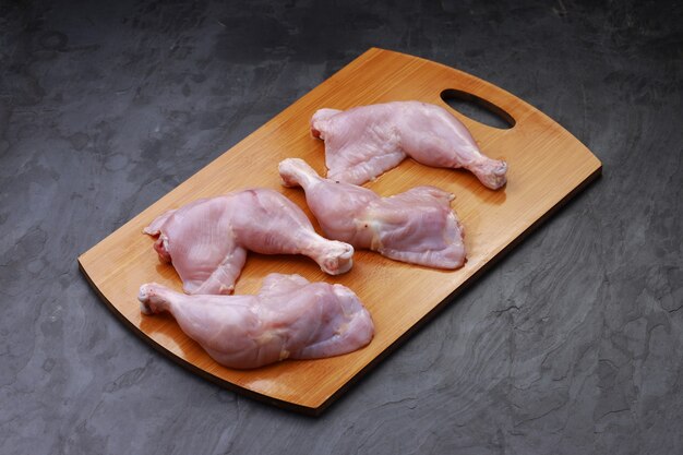 Coscia di pollo cruda o coscia di pollo disposta su una base di legno posta su uno sfondo di colore grigio