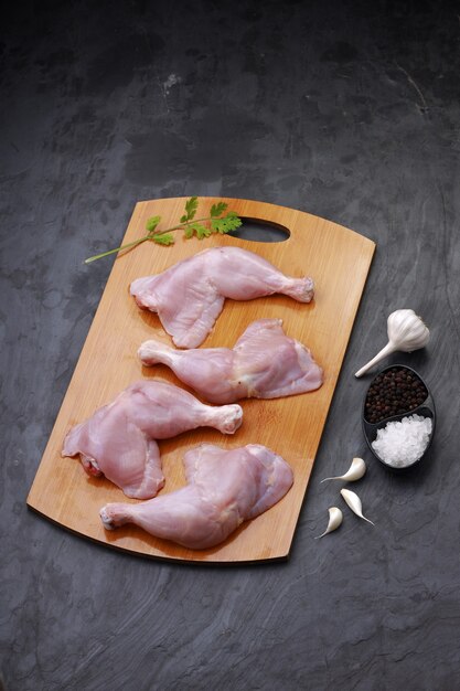 Coscia di pollo cruda o coscia di pollo disposta su una base di legno posta su uno sfondo di colore grigio