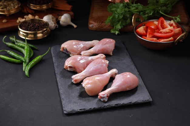 Coscia di pollo cruda o pezzi di coscia disposti su un foglio di grafite con ingredienti da cucina