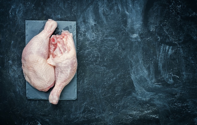 Coscia di pollo cruda sul piatto di pietra nero.