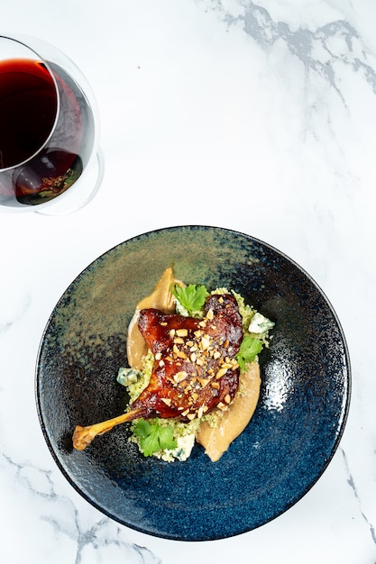 Cosciotto d'anatra confit con burro di arachidi e formaggio blu dor in elegante ciotola scura sul tavolo di marmo. Pranzo gourmet. Cucina francese.