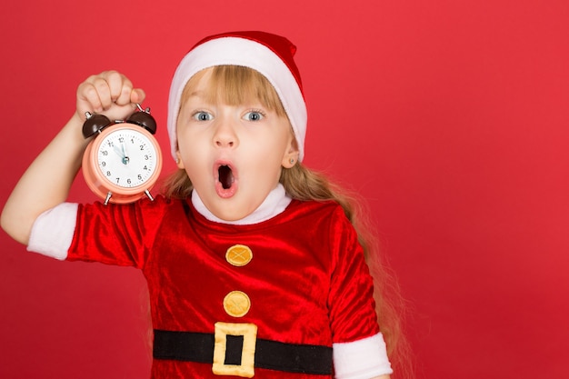 Così tanto da fare così poco tempo. Bambina indossa abiti di Natale urlando con sorpresa tenendo l'orologio in mano