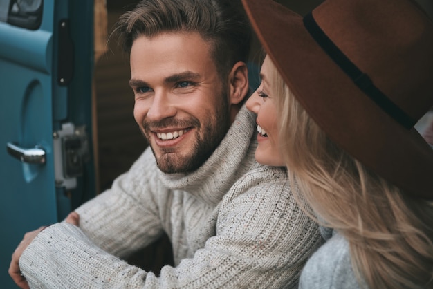 Così vicino. Belle giovani coppie che sorridono mentre sedendosi nel mini furgone blu di stile retrò