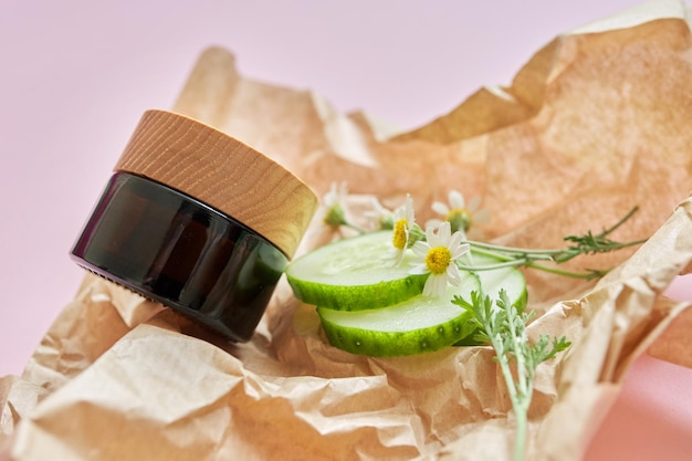 Cosmetici biologici a base di erbe medicinali, ingredienti naturali fiori di camomilla cetriolo, carta artigianale sfondo rosa, vista dall'alto