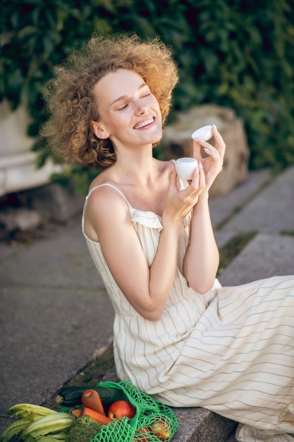 Cosmetici biologici. Bella donna seduta sui gradini con un vasetto di crema per il viso biologica nelle mani