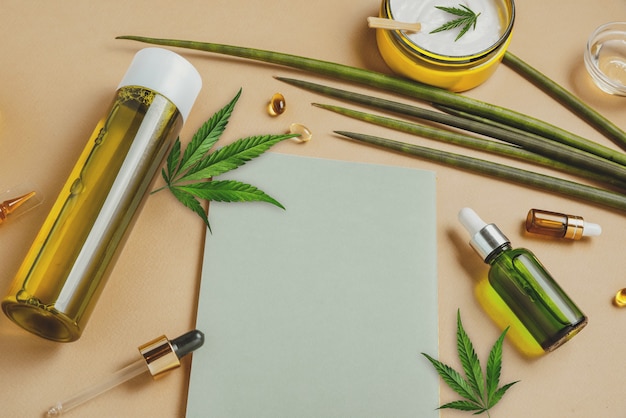 Cosmetici con olio di canapa CBD su una superficie beige con taccuino e foglie di marijuana