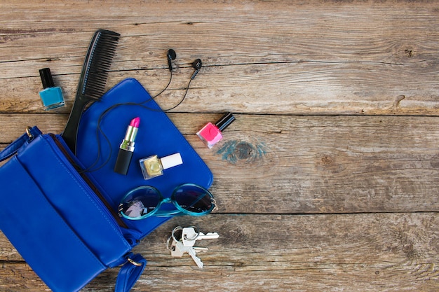 Cosmetici e accessori femminili sono caduti dalla borsetta blu. Vista dall&#39;alto.