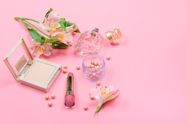 Cosmetici e fiori su una tavola rosa con copyspace