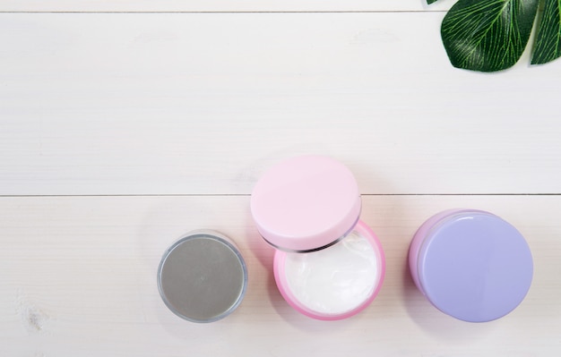 Cosmetici e prodotti per la cura della pelle e foglie verdi sul tavolo di legno bianco
