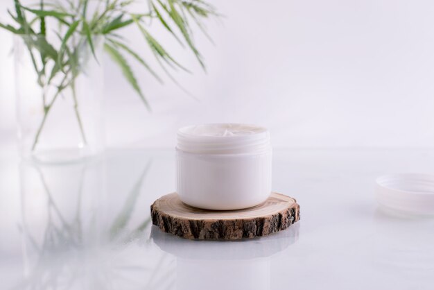 Cosmetici naturali con olio di cannabis. Barattolo bianco pulito con crema cosmetica e foglie verdi fresche di canapa.