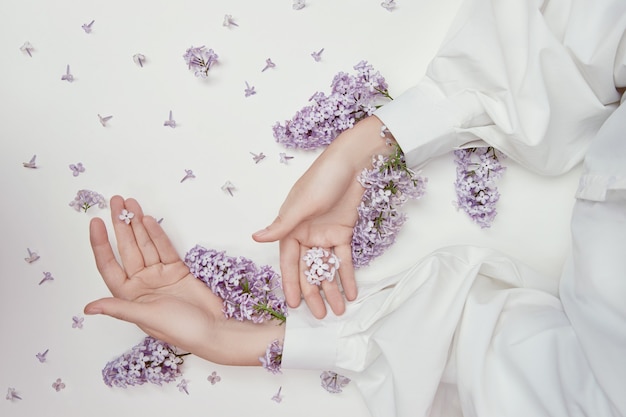 Cosmetici naturali da donna per mani realizzati con fiori e petali lilla. Idrata e ammorbidisce la pelle delle mani. Fiori lilla sporgono dalle maniche del braccio