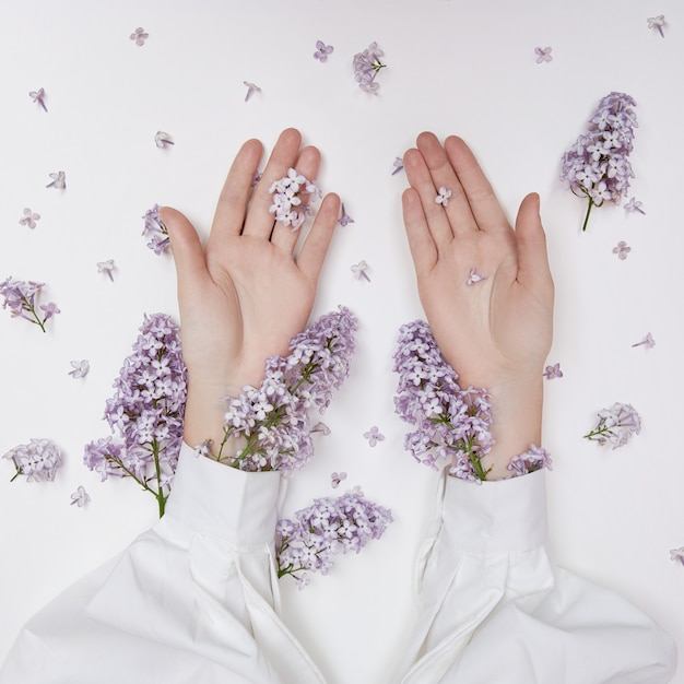 Cosmetici naturali da donna per mani realizzati con fiori e petali lilla. Idrata e ammorbidisce la pelle delle mani. Fiori lilla sporgono dalle maniche del braccio