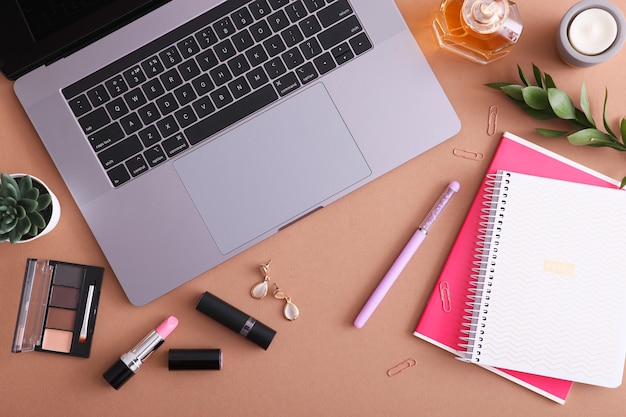 Cosmetici per il trucco e laptop moderno su una vista dall'alto di sfondo colorato