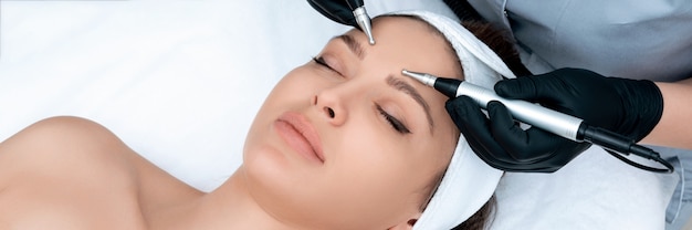 Cosmetologia. Bella donna alla clinica della stazione termale che riceve trattamento facciale elettrico stimolante dal terapista. Primo piano di giovane volto femminile durante la terapia microcorrente