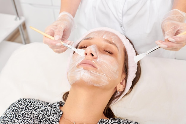 Cosmetologo che applica maschera crema cosmetica sul viso della donna per la procedura di ringiovanimento nel salone di bellezza