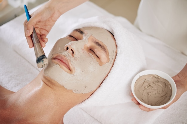 Cosmetologo che applica maschera purificante all'argilla