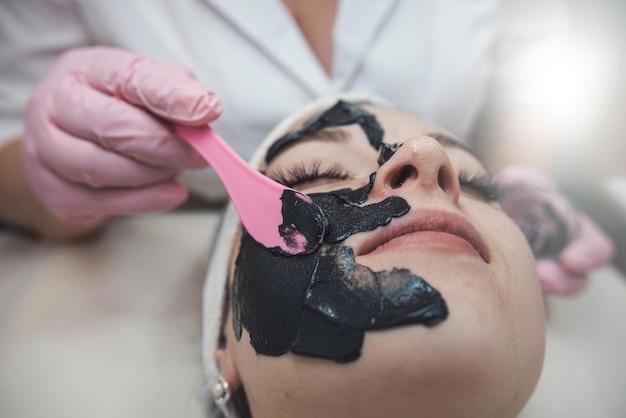 cosmetologo che applica una maschera di crema nera sul viso del suo cliente