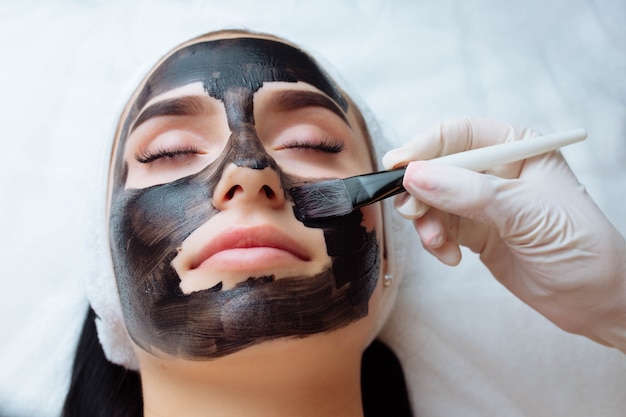 Cosmetologo che applica una maschera nera sul viso di una bella donna che indossa guanti neri splendida donna in spa h