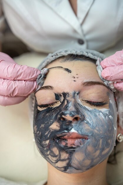 Cosmetologo che fa un massaggio lifting sul viso con maschera facciale ringiovanente la sua cliente femminile
