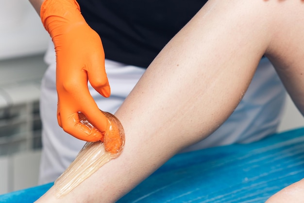 Cosmetologo donna che lavora con pasta di zucchero nella depilazione del primo piano del salone spa con pasta di zucchero