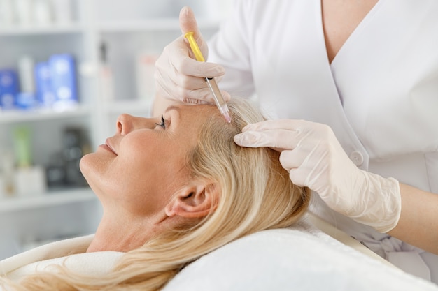 Cosmetologo fa terapia prp contro la caduta dei capelli di una donna bionda senior in un salone di bellezza.