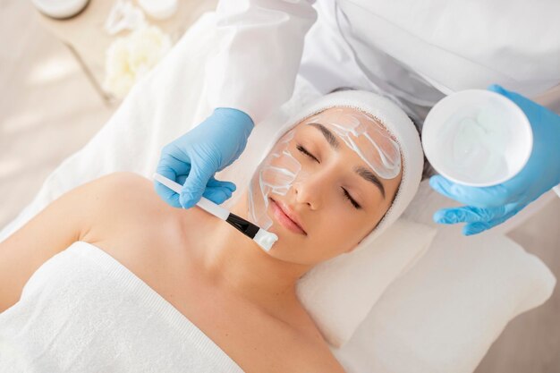 Cosmetologo per il trattamento della pelle che applica una maschera idratante sul viso di una giovane e bella donna