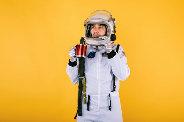 Cosmonauta maschio in tuta spaziale e casco con una tazza di caffè in mano, sulla parete gialla.