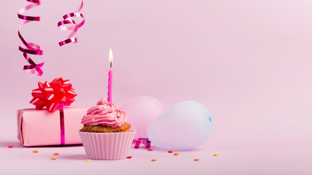 Cospargere la confezione regalo; palloncini e muffin con candela accesa su sfondo rosa