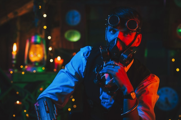 Cosplay post-apocalisse cyberpunk. Un uomo con gli occhiali e una maschera antigas in un'officina con una luce al neon