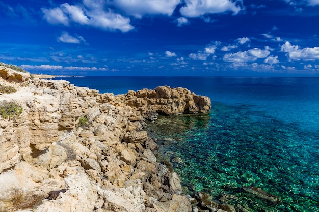 Costa del mare con acqua turchese chiaro, mantello di pietra, cielo blu con nuvole.