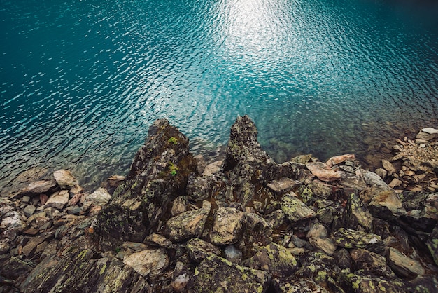 Costa rocciosa Bordo dell'acqua. Superficie lucida del lago di montagna azzurro. Fondo pietroso in acqua trasparente.