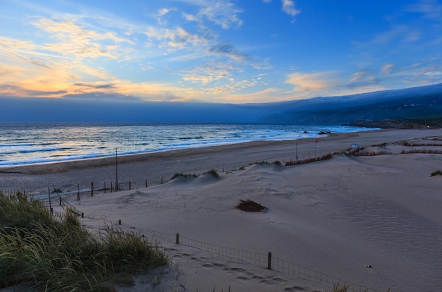 Costa rocciosa dell'Oceano Atlantico di estate di tramonto con la spiaggia sabbiosa (Guincho, Portogallo).