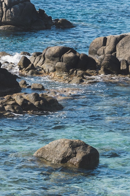 Costa selvaggia della spiaggia rocciosa e l'onda del mare schizza sulla roccia in riva al mare mare calmo che si infrangono le onde sulle rocce sulla riva creando schiuma di mare bianca