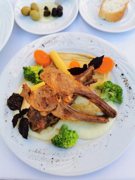 Costine con broccoli, carote e purè di patate su un piatto bianco deliziosa cena al ristorante