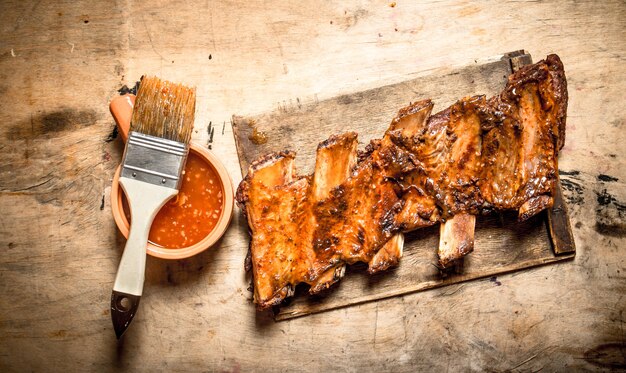 Costine di maiale affumicate con salsa piccante e un pennello sul tavolo di legno.