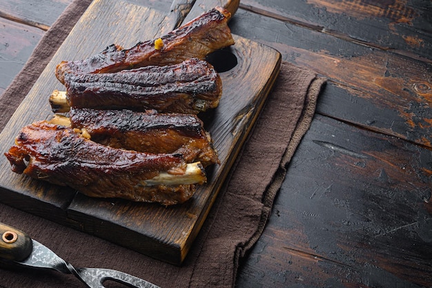 Costine di maiale alla griglia barbecue su tavola di legno con coltello da barbecue e forchetta di carne su sfondo vecchio tavolo in legno scuro