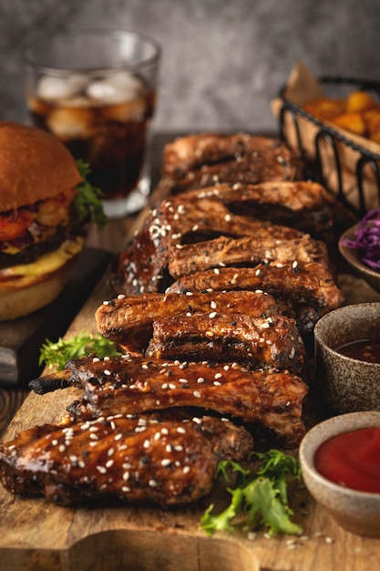 Costine di maiale barbecue su una tavola di legno, spicchi di patate, hamburger e bicchiere di cola, salsa. Fast food. Avvicinamento.