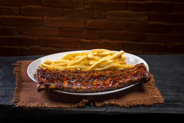 Costine di maiale con barbecue su tela marrone e legno nero su sfondo di mattoni.