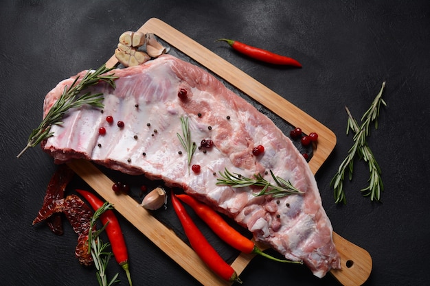 Costine di maiale crude intere. Carne suina fresca e ingredienti: spezie, sale e rosmarino su fondo scuro