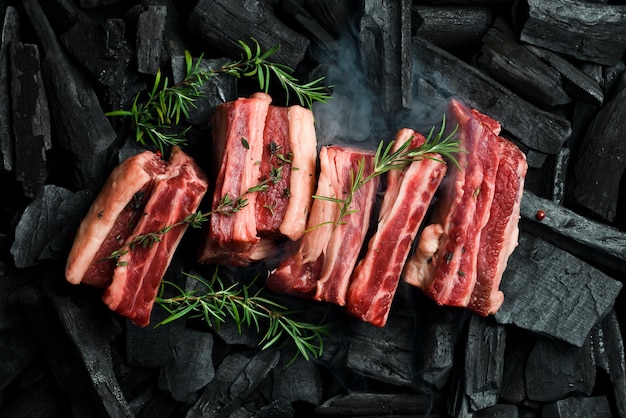 Costole di vitello crude fresche con rosmarino sui carboni Barbecue per la preparazione della carne Spazio libero per il testo