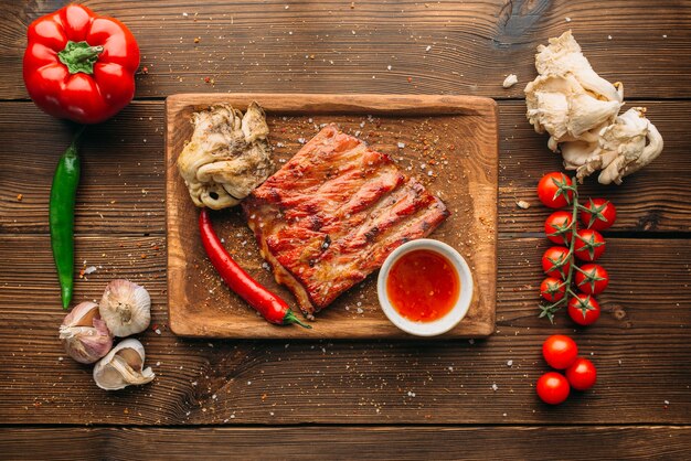 Costolette alla griglia succose e pezzo di carne sulla tavola di legno, vista dall'alto nessuno. Pepe, aglio ed erbe sullo sfondo