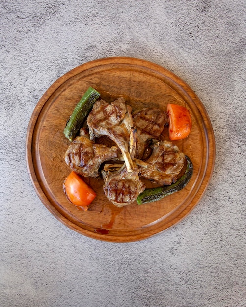 Costolette di agnello alla griglia su fondo di legno con peperoni arrostiti, pomodori e cipolle