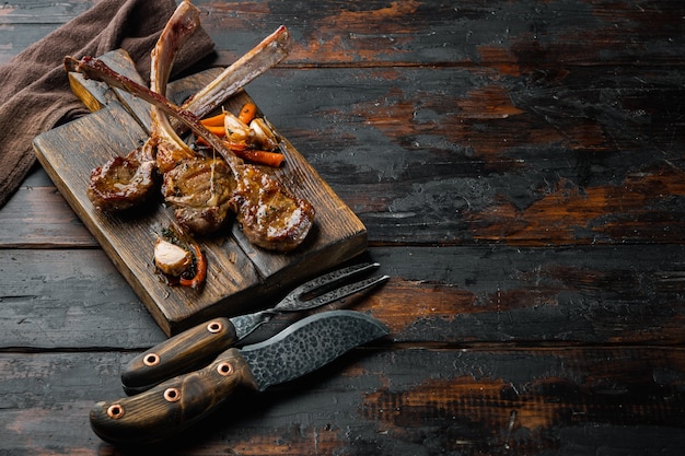 Costolette di agnello appiccicose con arancia e carota insieme, sul tagliere di legno, sul vecchio tavolo di legno scuro