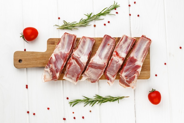 Costolette di carne cruda su tavola di legno su sfondo bianco