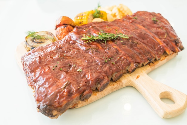 Costolette di maiale alla griglia con salsa barbecue e verdure e patatine frech sul tagliere in legno