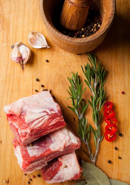 Costolette di maiale cruda su tavola tagliata con aglio pepe rosmarino e foglia di alloro Maiale crudo con spezie